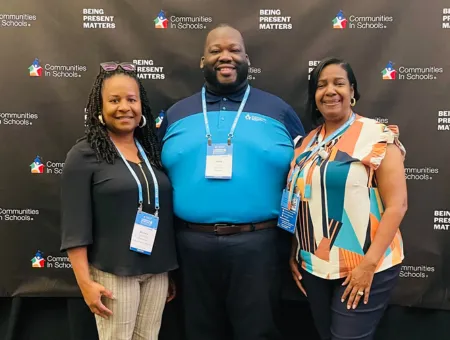 CIS of Baytown's Program Director and Executive Director standing beside Alumnus Malik with a black backdrop featuring the CIS logo