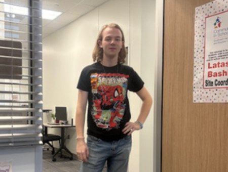 Leland standing in the CIS office doorway, wearing a graphic T-shirt, jeans, and boots.