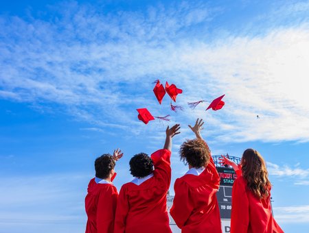 Four students throwing their red caps in the air