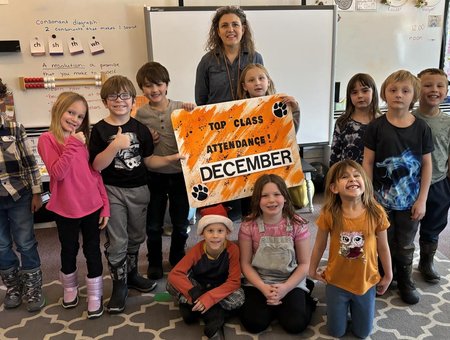 Classroom of teacher and students holding a top attendance sign